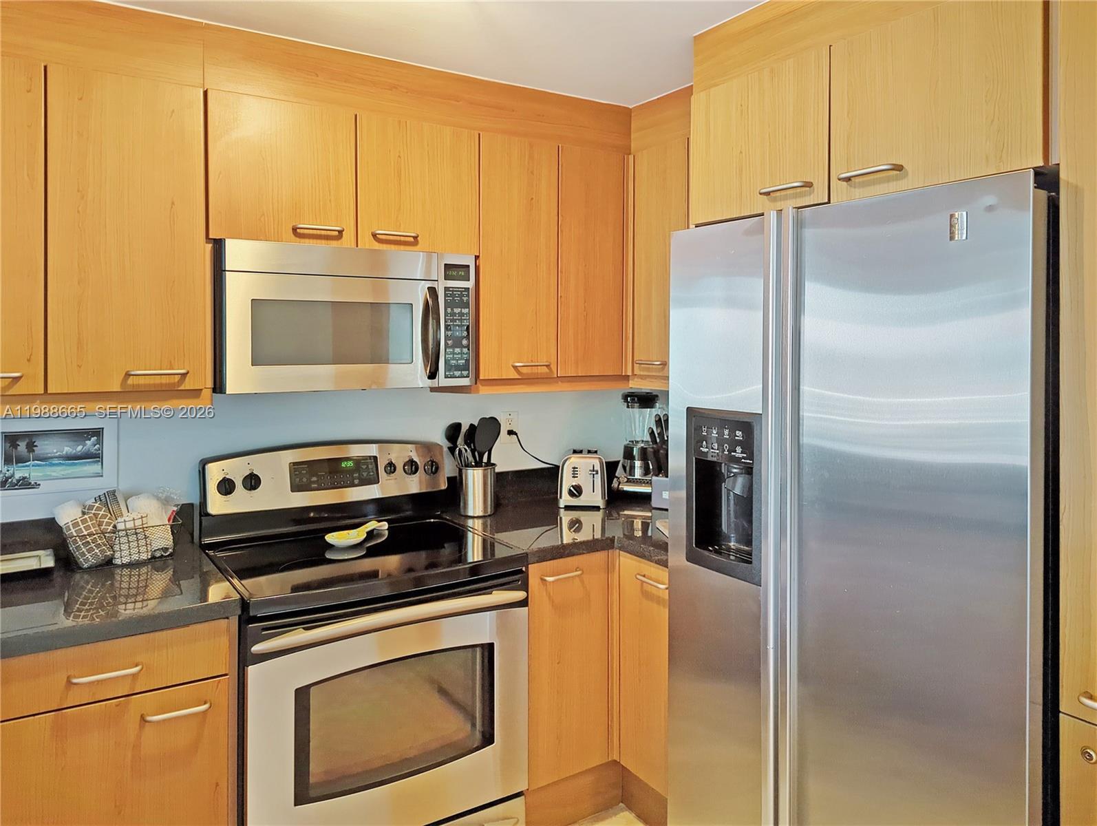 A kitchen features light wood cabinets, stainless steel appliances, and dark granite countertops — 225 Collins Ave # 4J, Miami Beach FL 33139, MIAMI BEACH, FL