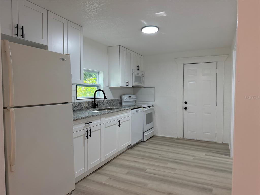 A kitchen features white cabinets, granite countertops, stainless steel appliances, and light wood-look flooring — 3403 LINDELL AVENUE, TAMPA, FL