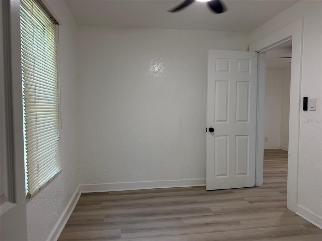 An empty room features white walls, light wood-look flooring, a window with blinds, and a doorway — 3403 LINDELL AVENUE, TAMPA, FL