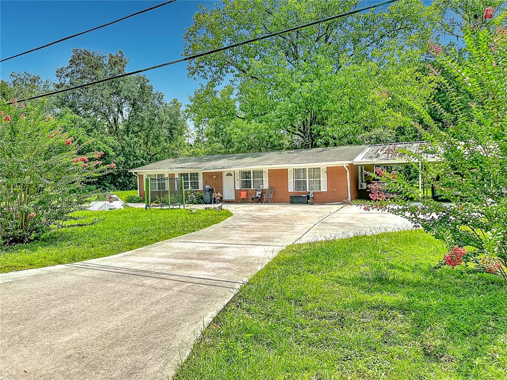 A single-story brick house with a concrete driveway, a carport, and a large front yard — 173 SE ANDREWS DRIVE, LAKE CITY, FL