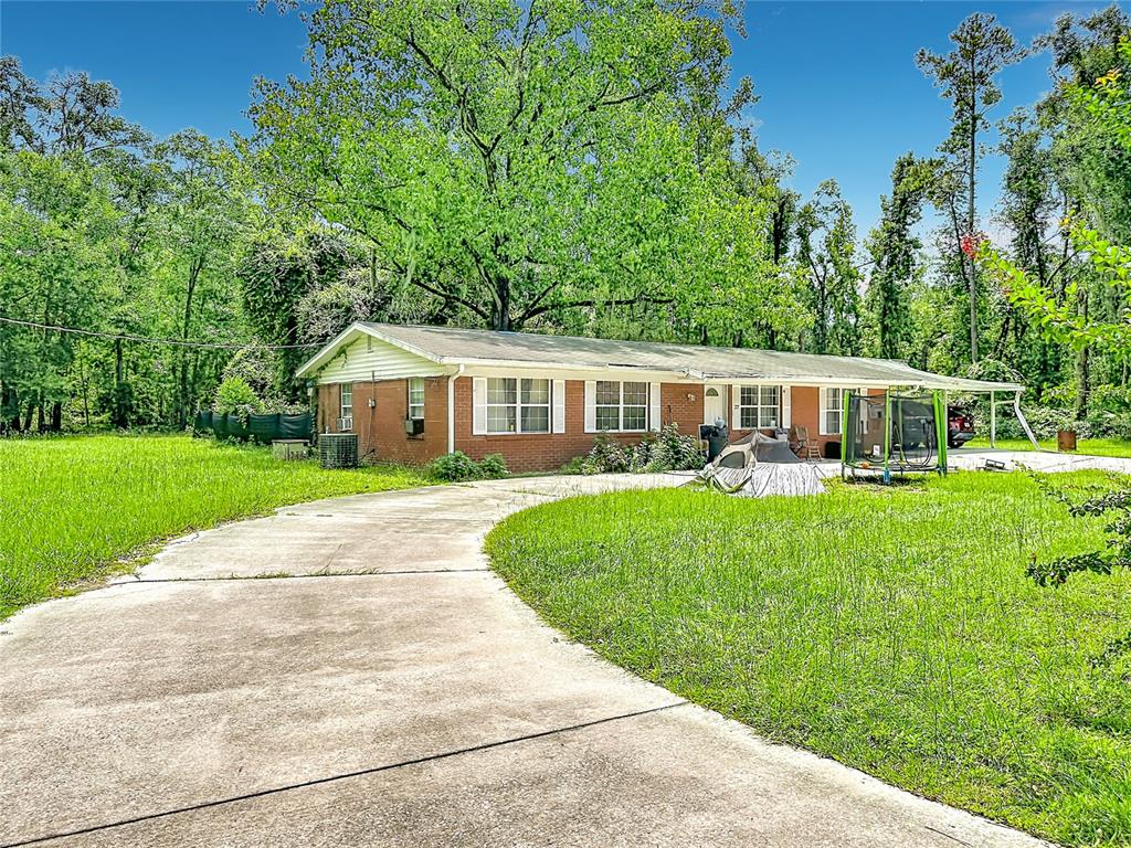 A single-story brick house with a concrete driveway, a large tree, and a grassy yard — 173 SE ANDREWS DRIVE, LAKE CITY, FL