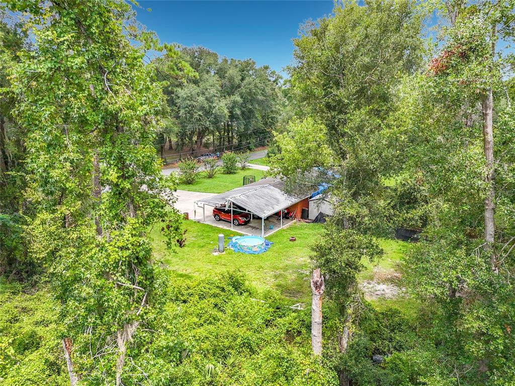 An aerial view shows a house with a metal carport, a small pool, and surrounding trees — 173 SE ANDREWS DRIVE, LAKE CITY, FL