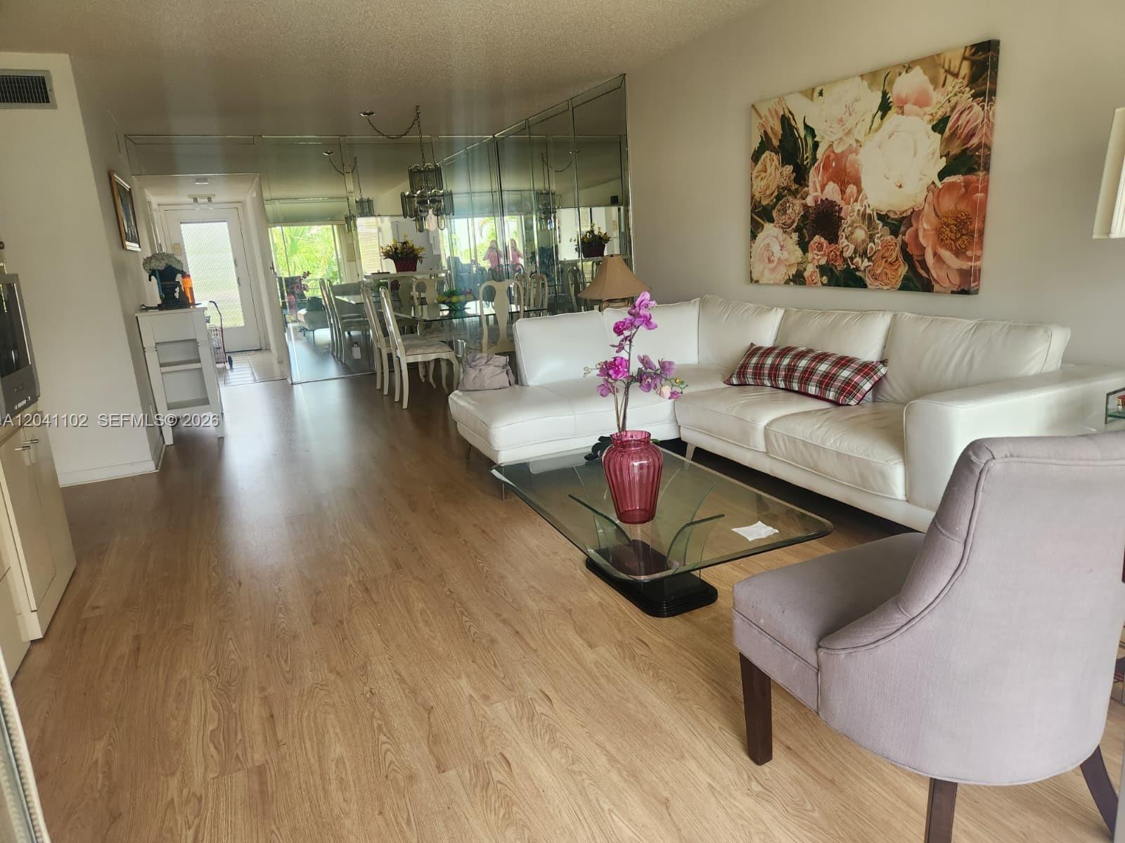 A living room features a white sectional sofa, glass coffee table, and mirrored dining wall — 3571 Inverrary Dr # 307, Lauderhill FL 33319, LAUDERHILL, FL