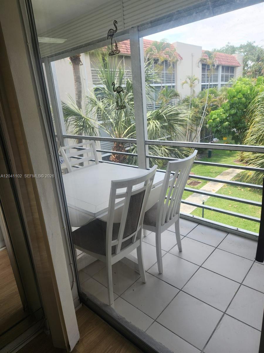 A balcony features a white dining set, tiled flooring, and a view of palm trees — 3571 Inverrary Dr # 307, Lauderhill FL 33319, LAUDERHILL, FL