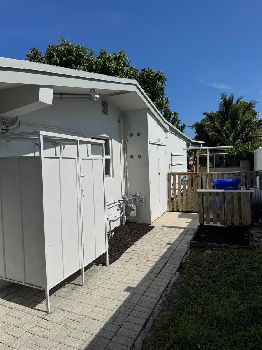A paved walkway leads past an outdoor shower enclosure toward a wooden gate and fence — 2560 NE 20th Street, Pompano Beach FL 33062, POMPANO BEACH, FL