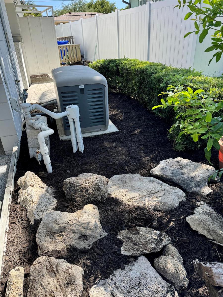 A backyard area features a large generator, white PVC piping, landscaping rocks, and a hedge — 2560 NE 20th Street, Pompano Beach FL 33062, POMPANO BEACH, FL
