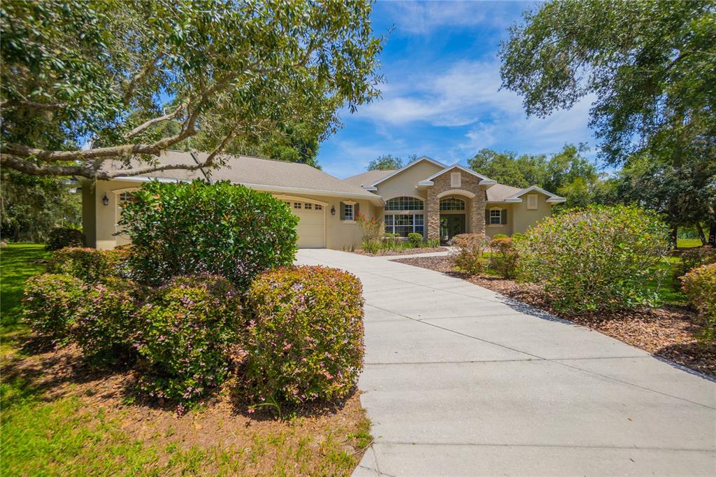 A single-story house with a stone-accented entryway, a concrete driveway, and surrounding trees — 9807 E LAKE TAHOE DRIVE, INVERNESS, FL