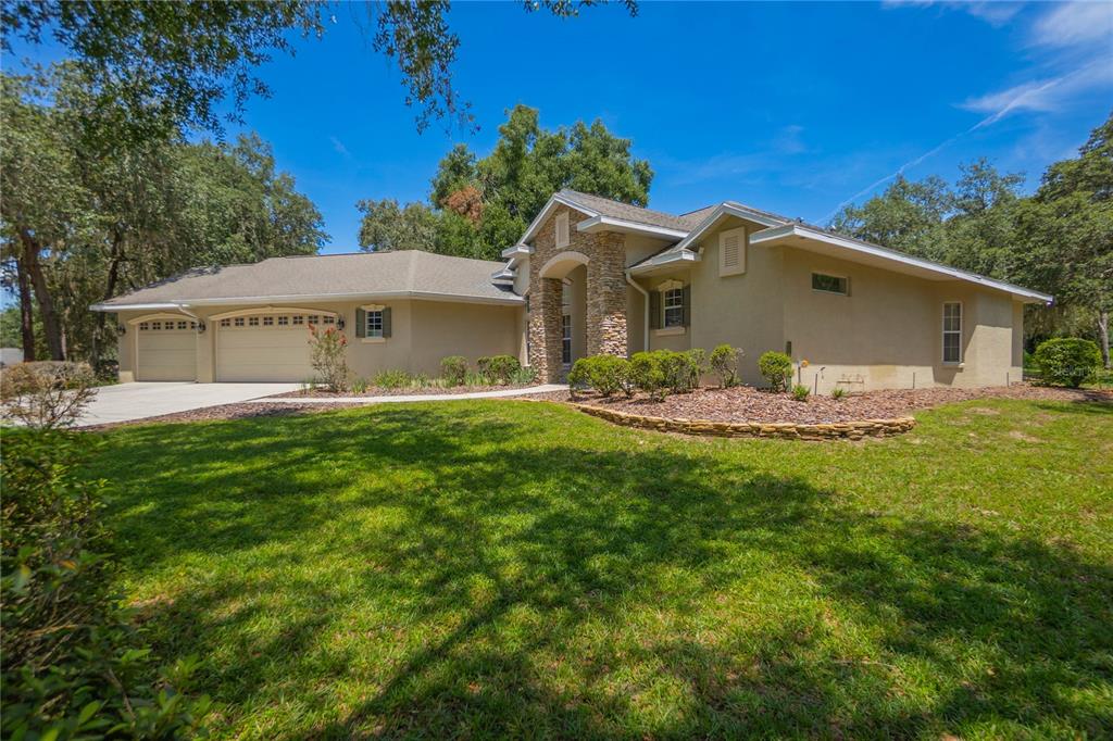 A single-story house with a stone-accented entryway, a three-car garage, and a landscaped front yard — 9807 E LAKE TAHOE DRIVE, INVERNESS, FL