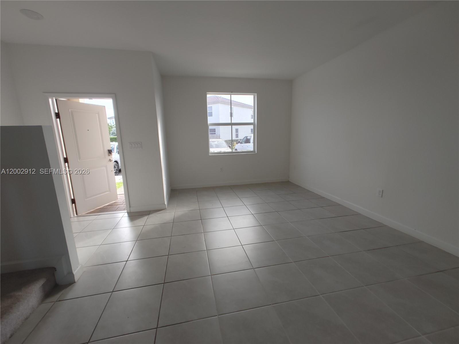 An empty room features white walls, light-colored tile flooring, a window, and an open door — 2353 NW 122nd Ter # 0, Miami FL 33167, MIAMI, FL