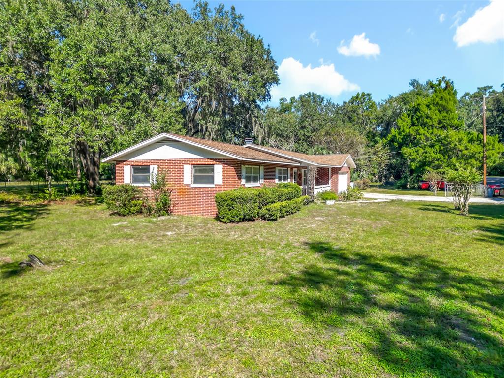 A single-story brick house with a gabled roof sits on a grassy, tree-filled lot — 7802 MIZELL STREET, COLEMAN, FL