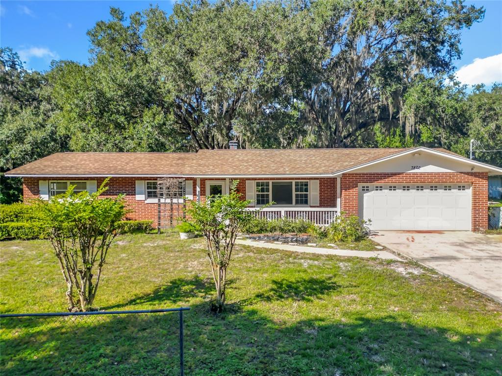 A single-story brick house with a white garage door and a large tree in front — 7802 MIZELL STREET, COLEMAN, FL