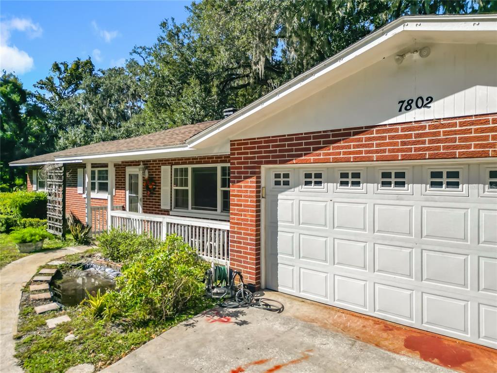 A single-story brick house features a white garage door, a front porch, and a pond — 7802 MIZELL STREET, COLEMAN, FL