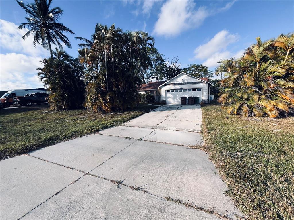 A single-story house with a white garage door and a concrete driveway sits among palm trees — 2247 SW 4TH STREET, CAPE CORAL, FL