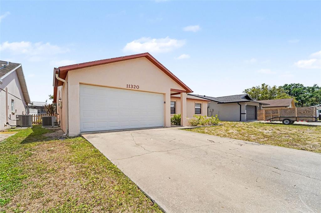 A single-story house with a beige stucco exterior, a white garage door, and a concrete driveway — 11320 JACK RABBIT LANE, PORT RICHEY, FL