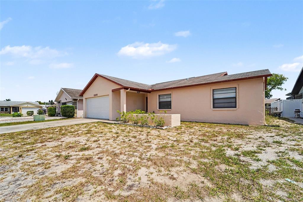 A single-story peach-colored house with a garage and a sparse, sandy front yard — 11320 JACK RABBIT LANE, PORT RICHEY, FL