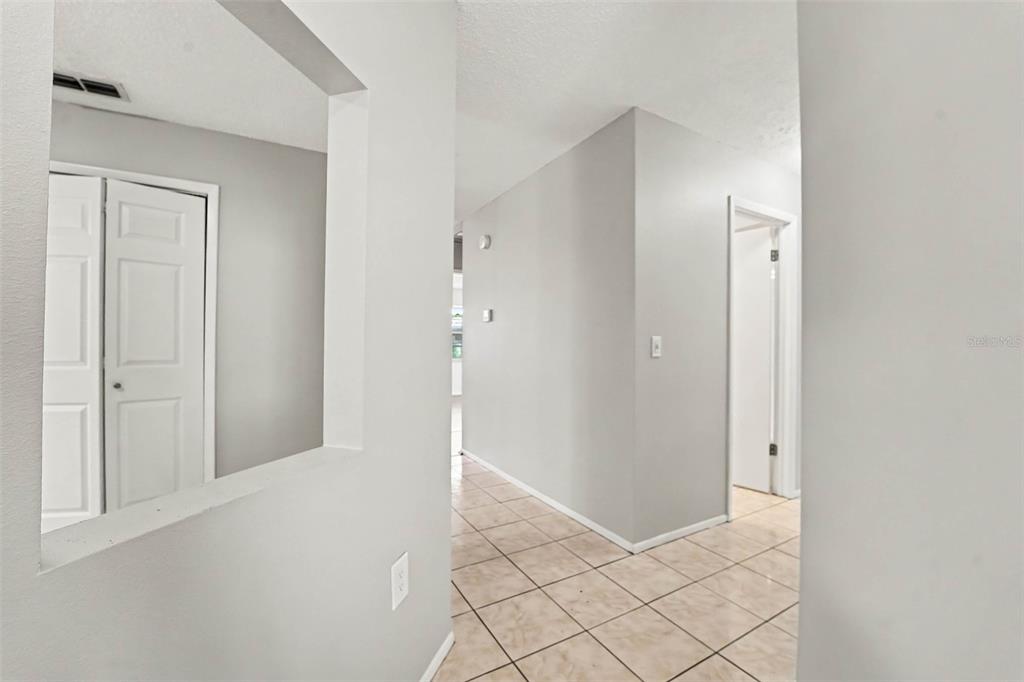 A hallway with light-colored tile flooring leads toward an open doorway — 11320 JACK RABBIT LANE, PORT RICHEY, FL