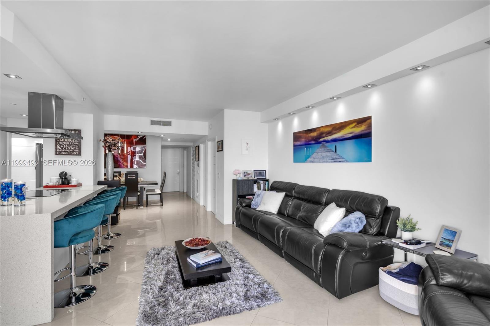 A modern living room features a black leather sofa, a kitchen island with barstools, and tile flooring — 4775 Collins Ave # 3608, Miami Beach FL 33140, MIAMI BEACH, FL
