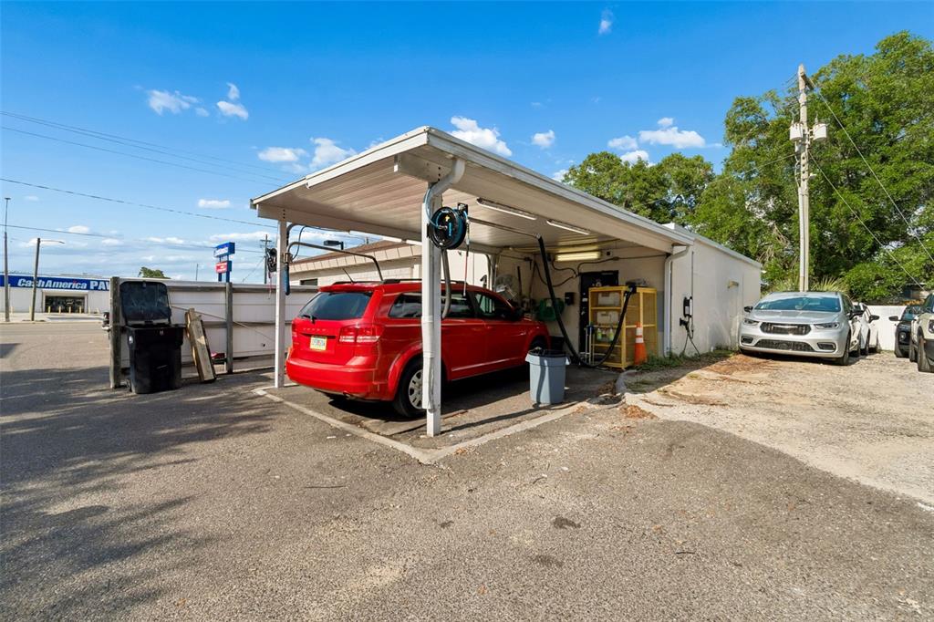 A red SUV is parked under a covered outdoor service bay next to a building — 4901 E BUSCH BOULEVARD, TAMPA, FL