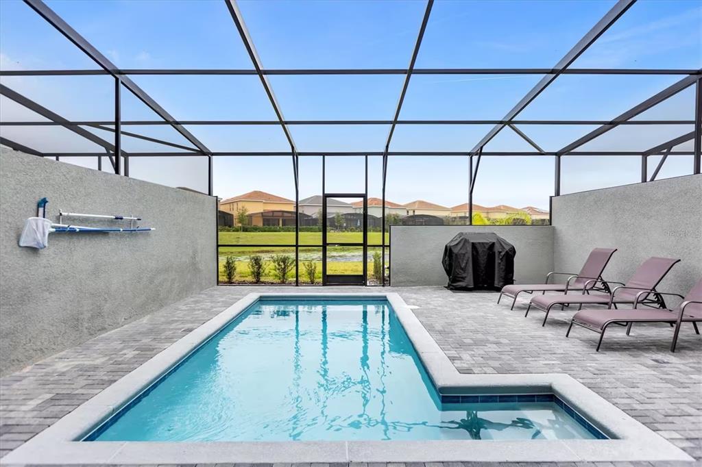A screened-in patio features a rectangular swimming pool, lounge chairs, and a grill — 7542 OAK SPRING LANE, DAVENPORT, FL
