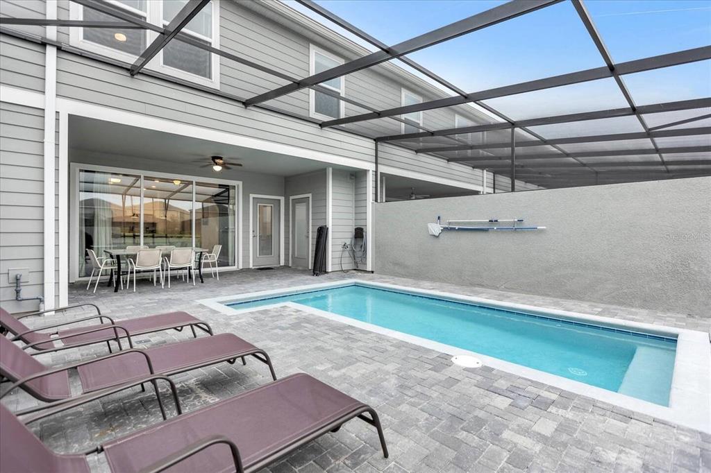 A screened-in patio features a rectangular swimming pool, lounge chairs, and a dining set — 7542 OAK SPRING LANE, DAVENPORT, FL