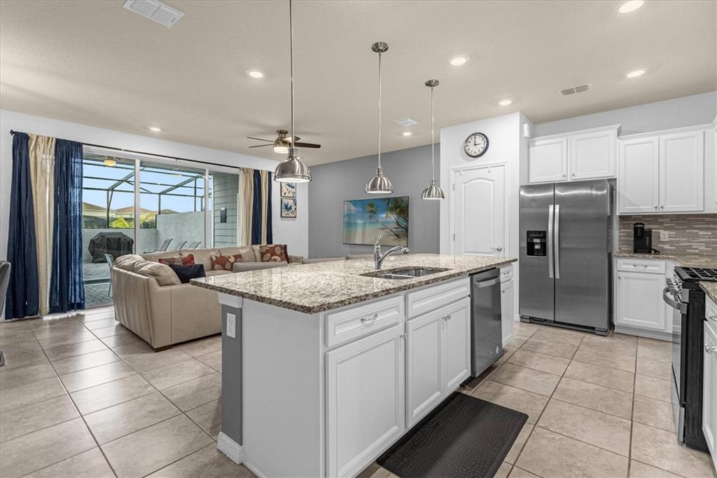 A kitchen with a granite-topped island and stainless steel appliances overlooks a living room area — 7542 OAK SPRING LANE, DAVENPORT, FL