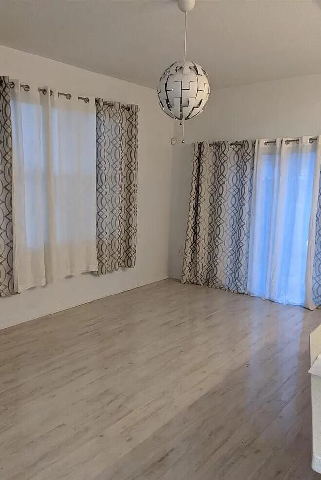 A bright room features light wood-look flooring, patterned curtains, and a modern spherical pendant light — 1655 NE 33rd Road # 4, Homestead FL 33033, HOMESTEAD, FL