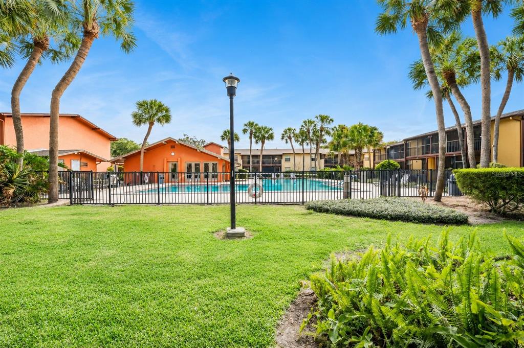 A grassy lawn leads to a fenced swimming pool area surrounded by palm trees and buildings — 754 E MICHIGAN STREET UNIT 185, ORLANDO, FL