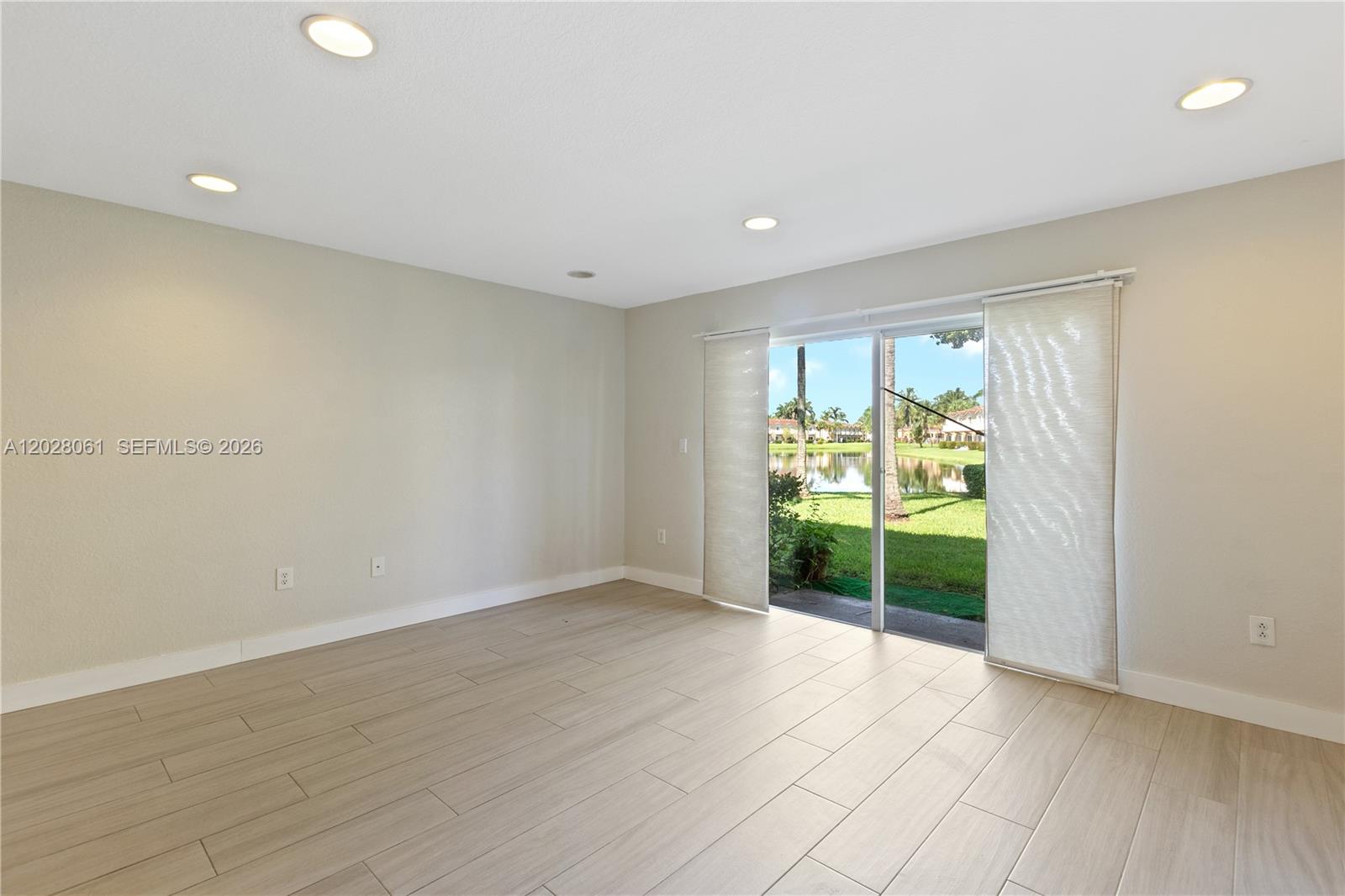 An empty room features light-colored tile flooring, recessed lighting, and sliding glass doors overlooking a lake — 3126 SW 128th Ave # 157, Miramar FL 33027, MIRAMAR, FL