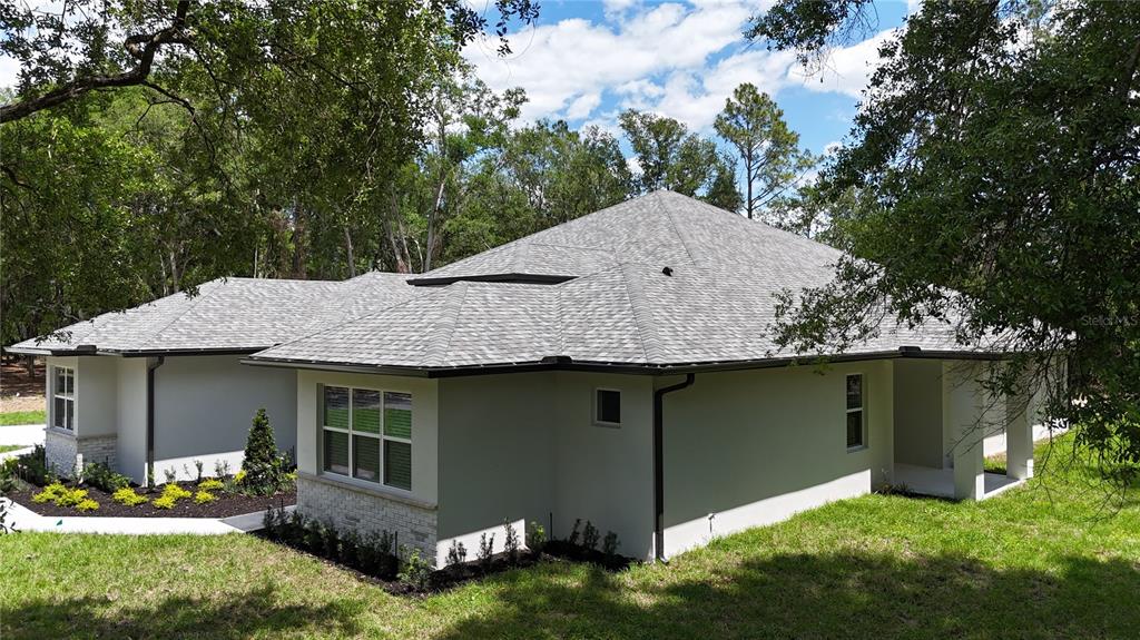 A side view of a light-colored house with a gray shingled roof and landscaping — 24950 BONSMARA DRIVE, GROVELAND, FL