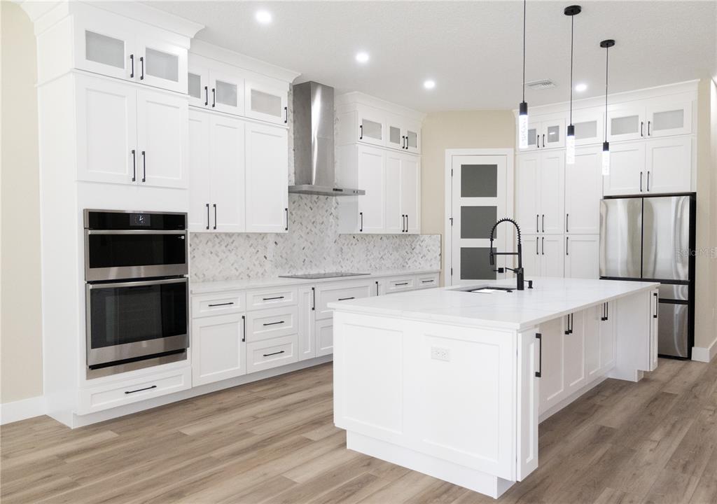 A modern kitchen features white cabinetry, stainless steel appliances, a marble backsplash, and a large island — 24950 BONSMARA DRIVE, GROVELAND, FL