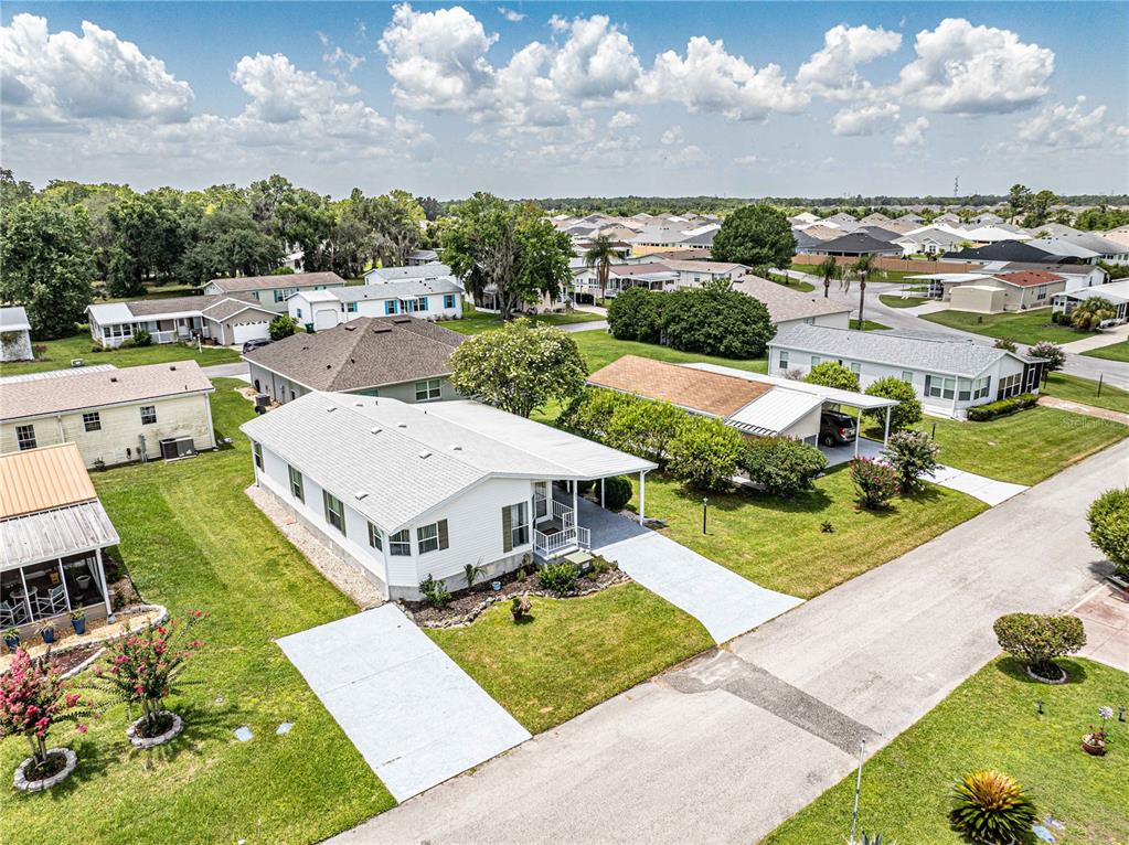 An aerial view shows a white manufactured home with a carport in a residential neighborhood — 5217 CAMBRIDGE COURT, WILDWOOD, FL