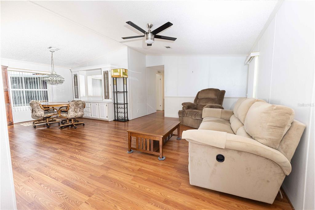 A living and dining area with wood-look flooring, a ceiling fan, and beige furniture — 5217 CAMBRIDGE COURT, WILDWOOD, FL