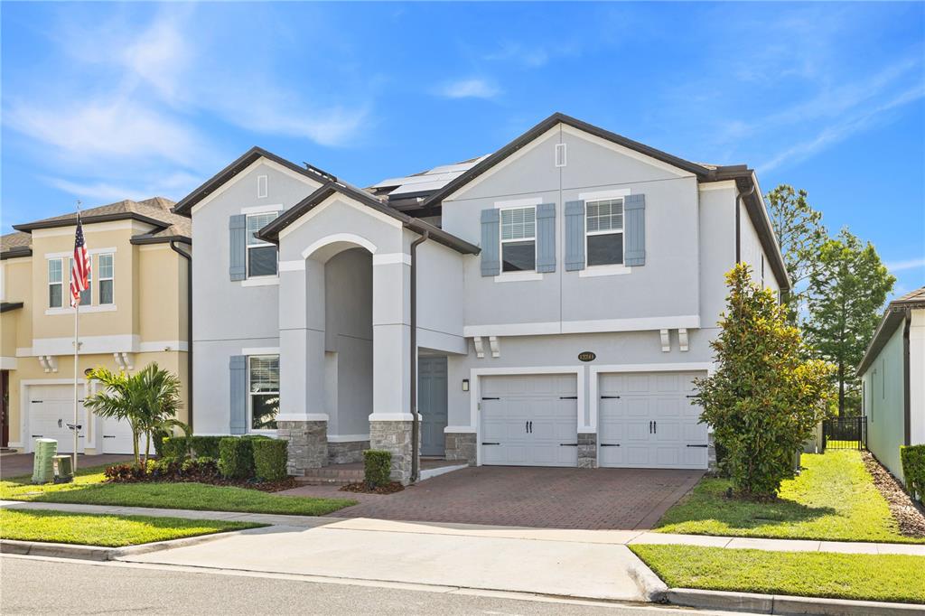 A two-story suburban house with a gray stucco exterior, stone accents, and a two-car garage — 12241 ENCORE AT OVATION WAY, WINTER GARDEN, FL