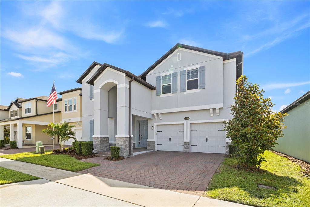A two-story house with a gray stucco exterior, stone accents, and a brick paver driveway — 12241 ENCORE AT OVATION WAY, WINTER GARDEN, FL