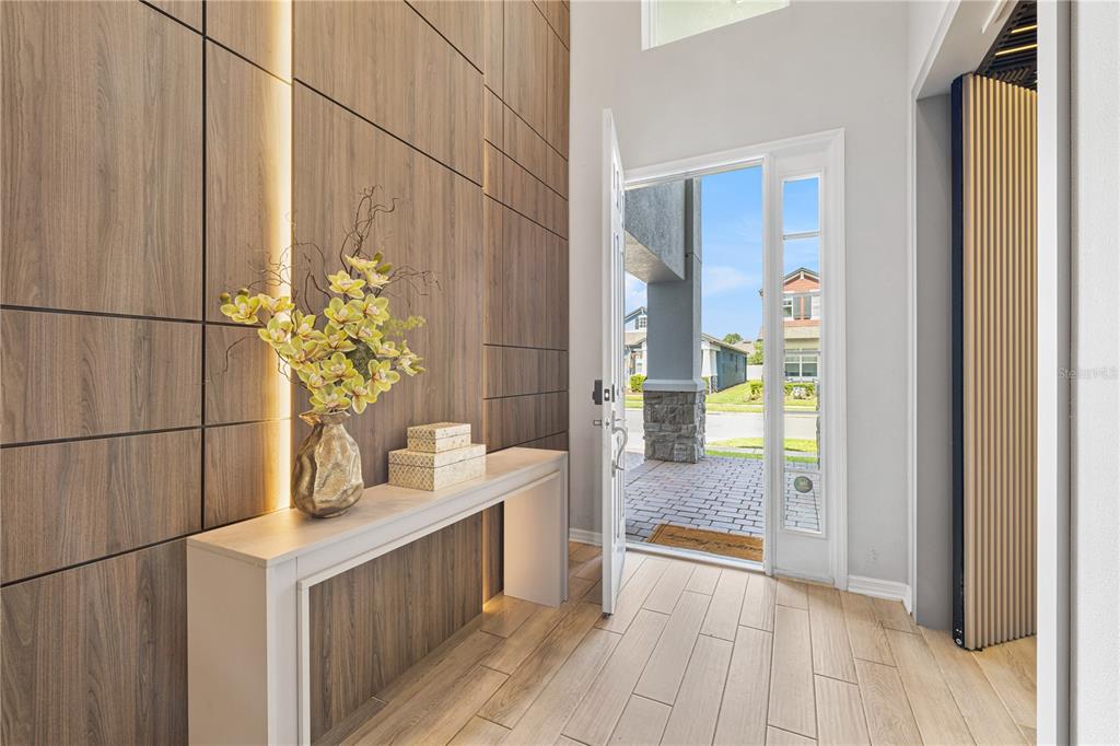 A modern entryway features a wood-paneled accent wall, a console table, and an open door — 12241 ENCORE AT OVATION WAY, WINTER GARDEN, FL