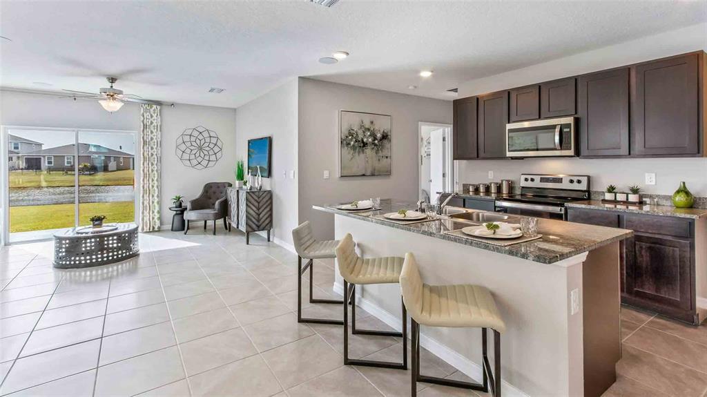 A kitchen with dark cabinets and a granite island overlooks a living area with tile — 32370 WEATHERED OAK DRIVE, WESLEY CHAPEL, FL