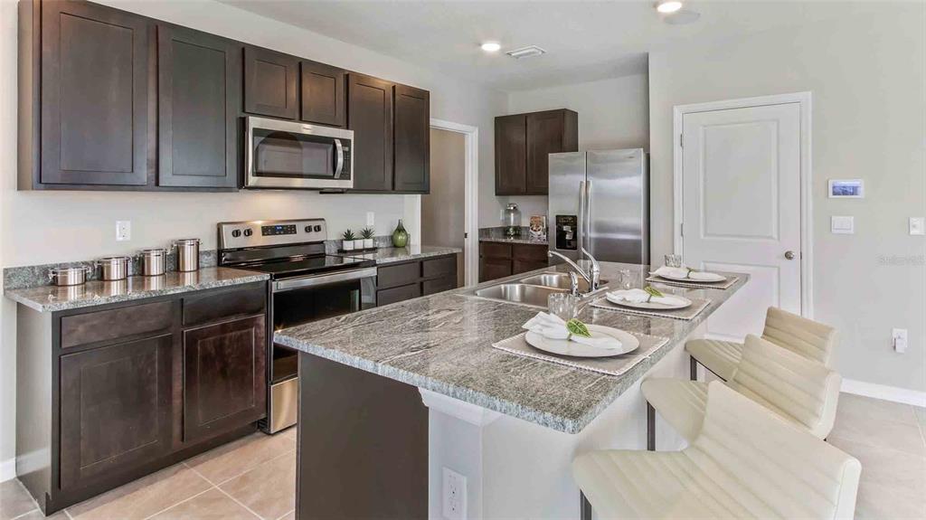 A kitchen features dark wood cabinets, granite countertops, stainless steel appliances, and a center island — 32370 WEATHERED OAK DRIVE, WESLEY CHAPEL, FL