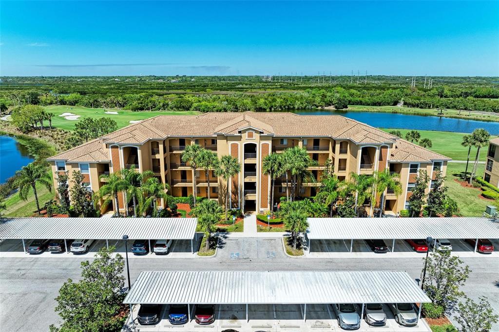 An aerial view of a multi-story apartment building with covered parking and a golf course — 8105 GRAND ESTUARY TRAIL UNIT 403, BRADENTON, FL