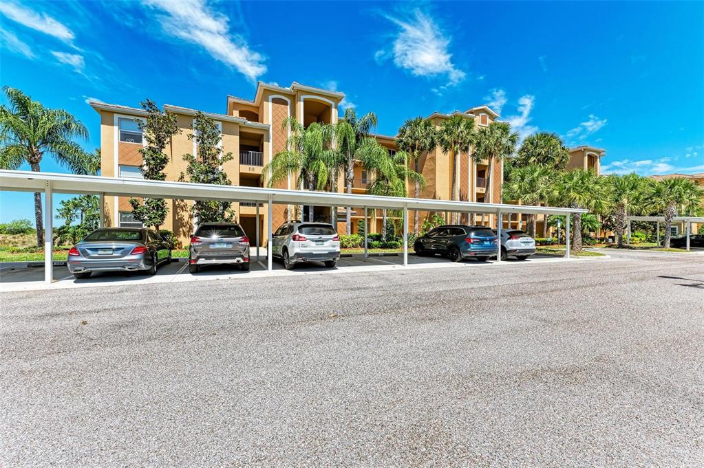 A multi-story apartment building with a covered parking area in front — 8105 GRAND ESTUARY TRAIL UNIT 403, BRADENTON, FL