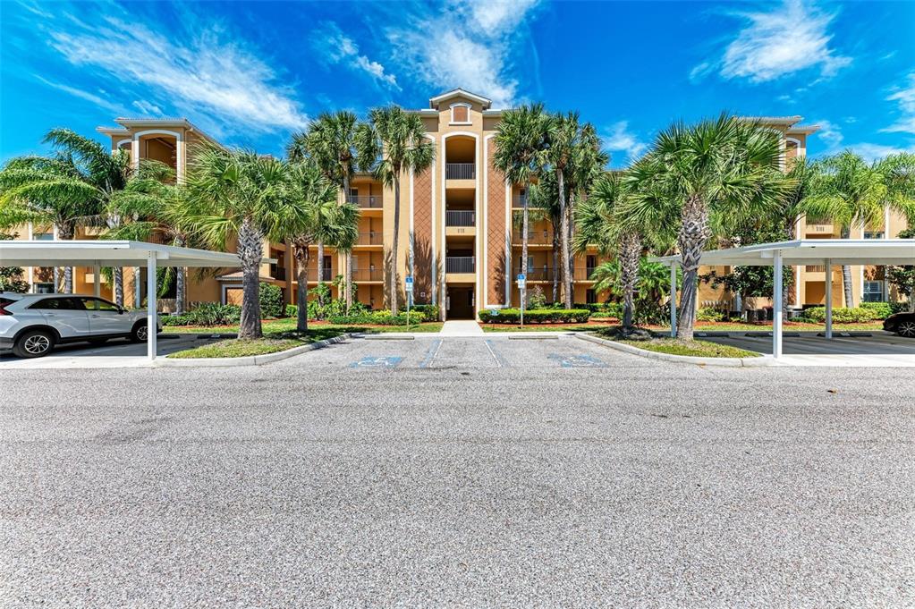 A multi-story apartment building with covered parking spaces and palm trees in the foreground — 8105 GRAND ESTUARY TRAIL UNIT 403, BRADENTON, FL