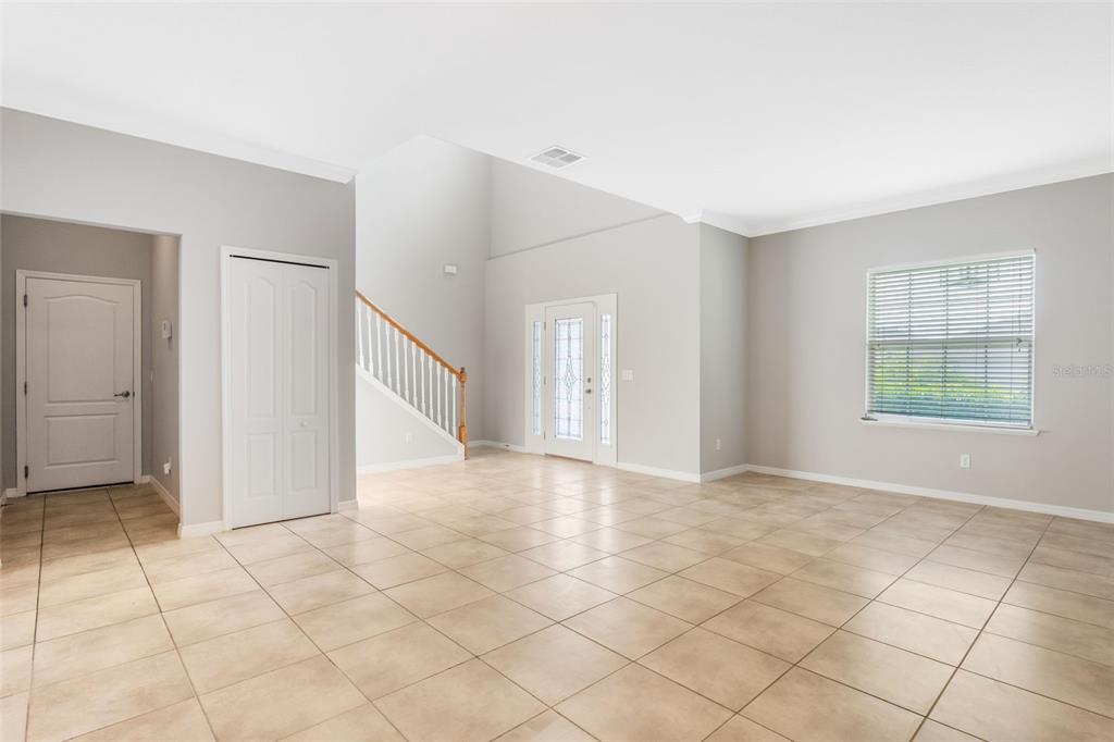 An empty living room features light tile flooring, gray walls, a staircase, and a front door — 1383 WATER WILLOW DRIVE, GROVELAND, FL