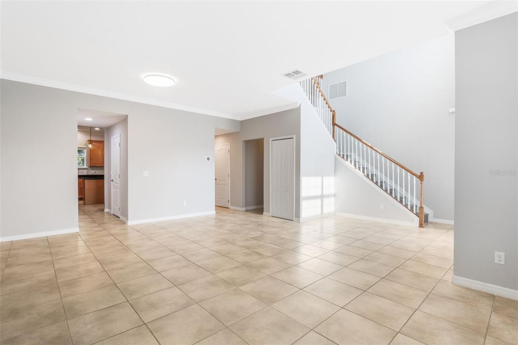 A spacious room with light-colored tile flooring, a staircase with white railings, and neutral walls — 1383 WATER WILLOW DRIVE, GROVELAND, FL