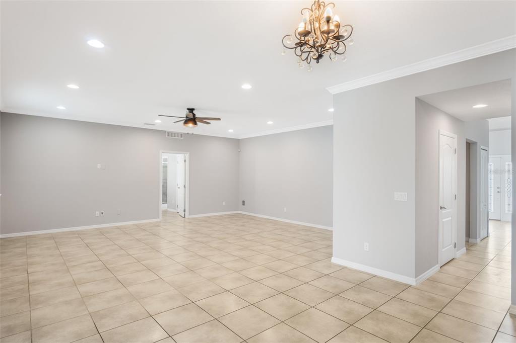 A spacious, empty room features light gray walls, beige tile flooring, a ceiling fan, and a chandelier — 1383 WATER WILLOW DRIVE, GROVELAND, FL
