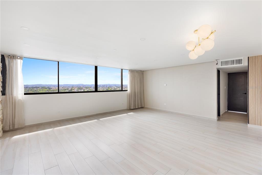 A bright, empty room features light wood-look flooring, a modern globe chandelier, and large windows — 2306 CALLE LAUREL UNIT 11-E, SAN JUAN, PR