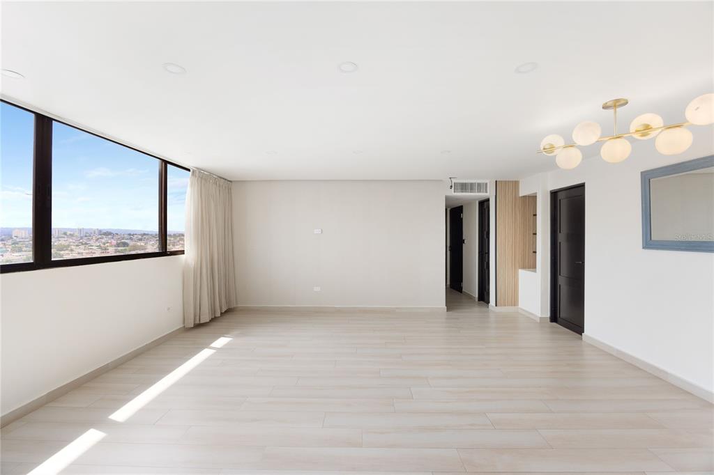 A bright, empty room features light wood-look flooring, a modern chandelier, and a large window — 2306 CALLE LAUREL UNIT 11-E, SAN JUAN, PR