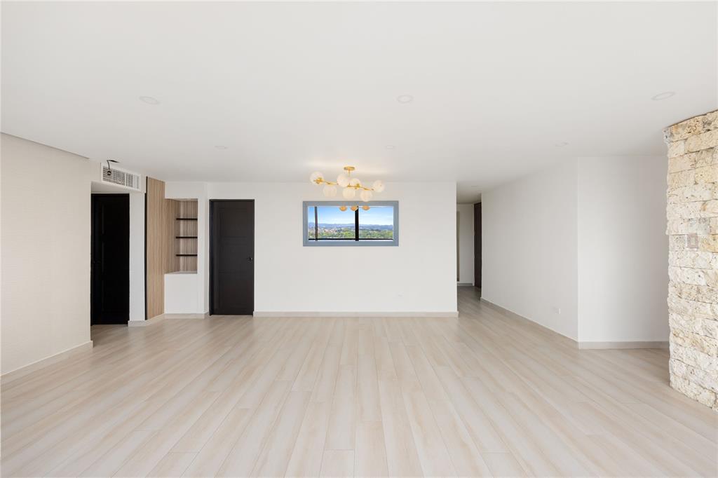 A spacious, minimalist room features light wood flooring, white walls, a stone pillar, and a window — 2306 CALLE LAUREL UNIT 11-E, SAN JUAN, PR