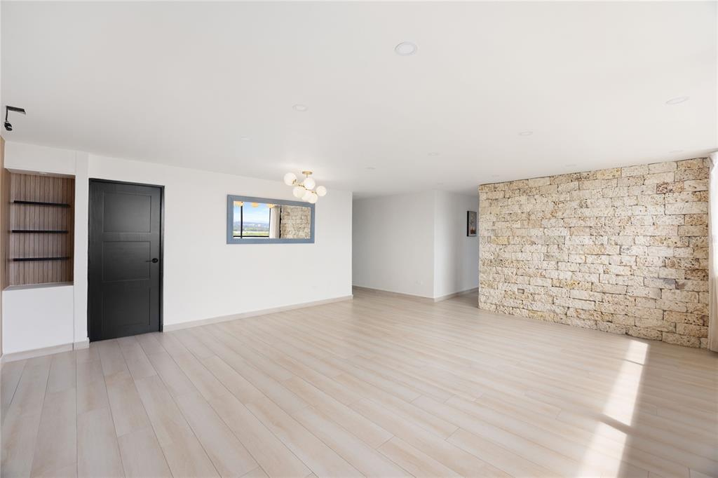 A bright, empty room features light wood flooring, a black door, and a stone accent wall — 2306 CALLE LAUREL UNIT 11-E, SAN JUAN, PR