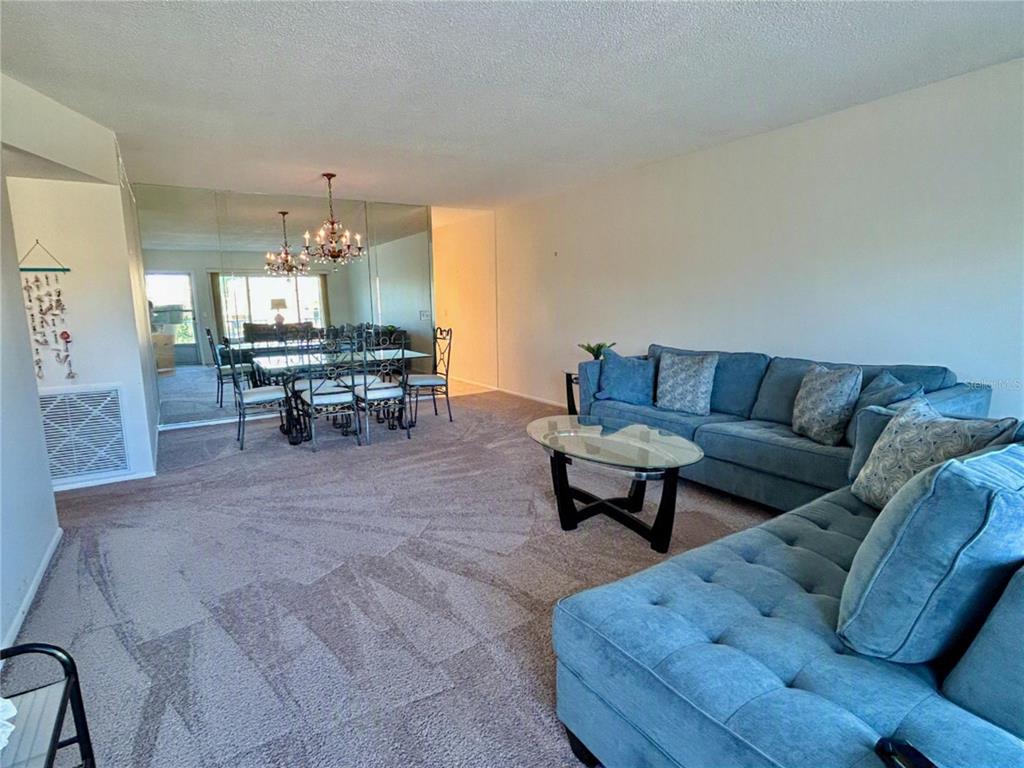 A living room with blue sectional seating, a glass coffee table, and a mirrored dining area — 2070 WORLD PARKWAY BOULEVARD UNIT 36, CLEARWATER, FL