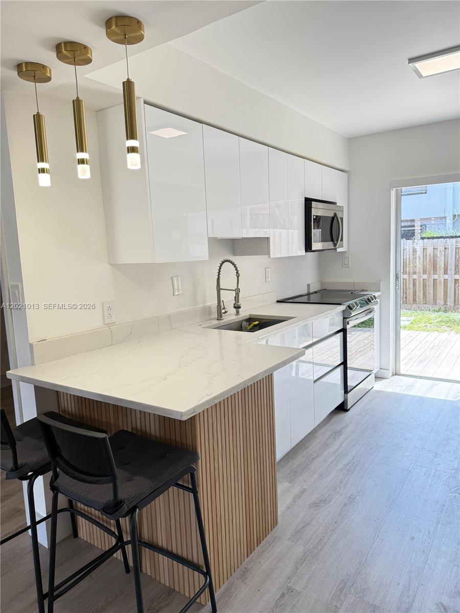 A modern kitchen features white glossy cabinets, a wood-slatted breakfast bar, and gold pendant lights — 15250 SW 80th St # 9, Miami FL 33193, MIAMI, FL
