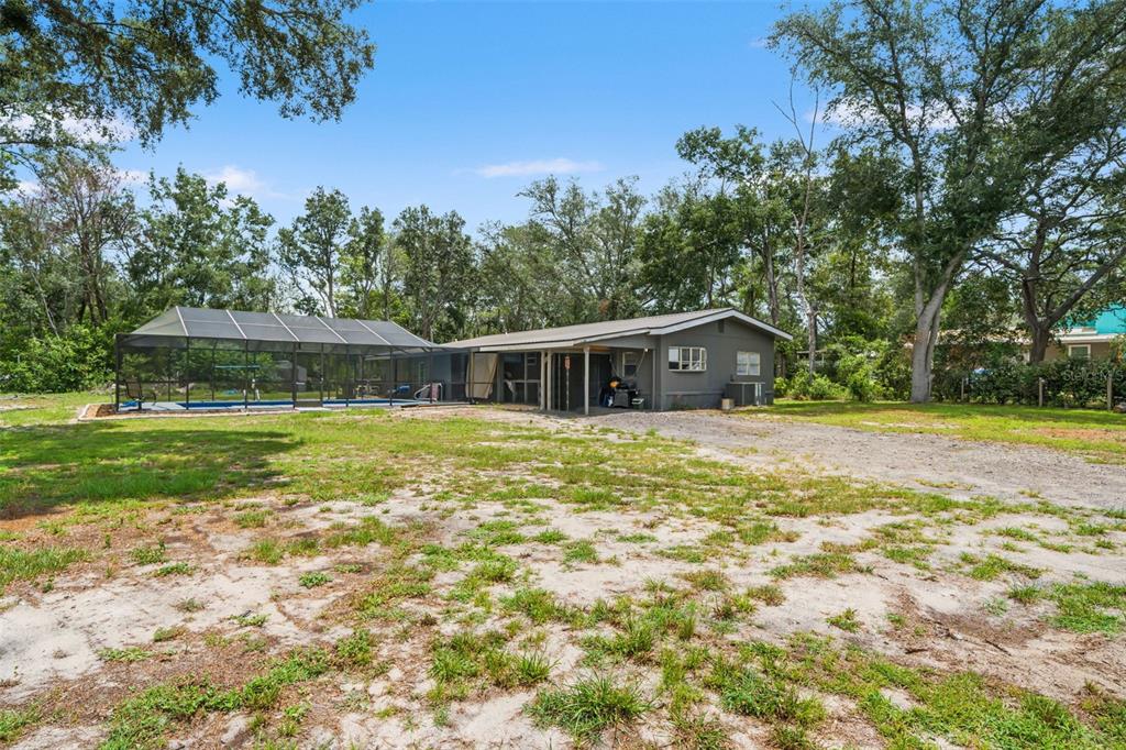 A gray house with a screened-in pool enclosure sits on a large, grassy lot — 8343 YELLOW PINE AVENUE, BROOKSVILLE, FL